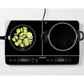 Black induction cooktop with a pan of zucchini and an empty pan on a white background