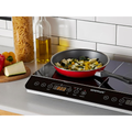 Induction cooktop with a frying pan containing vegetables on a kitchen counter.