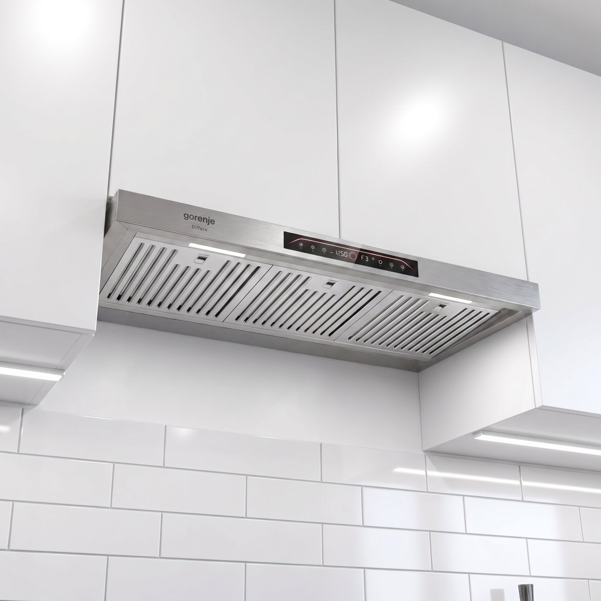 A stainless steel Gorenje range hood mounted under white kitchen cabinets above white subway tiles.