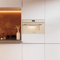 A built-in oven or microwave in a cream finish, installed in a modern white kitchen cabinet next to a copper mosaic tile backsplash.