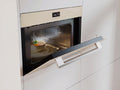A built-in microwave oven in a modern white kitchen, shown with its door open and a bowl of soup inside on a plate.