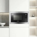 A built-in stainless steel and black microwave oven installed in a modern white kitchen cabinet, shown with side shelving and a countertop bowl in the background.