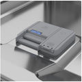 A gray automatic dishwasher detergent dispenser placed on the inside of a stainless steel dishwasher rack.