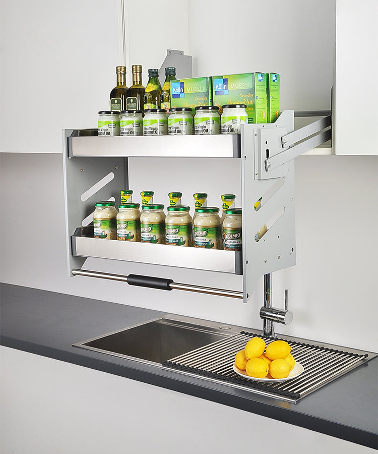 A stainless steel Kangyale elevator basket mounted on a wall above a kitchen sink, partially open with some kitchen towels inside.