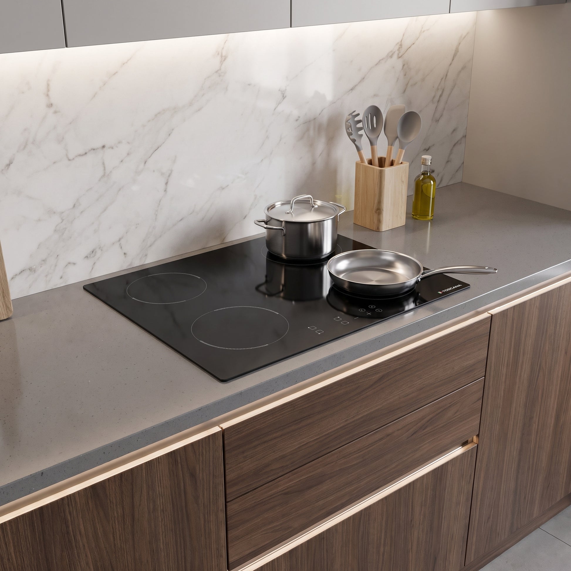 A modern kitchen countertop with a black induction cooktop, a stainless steel pot, and a frying pan, set against a white marble backsplash and dark wood cabinets.