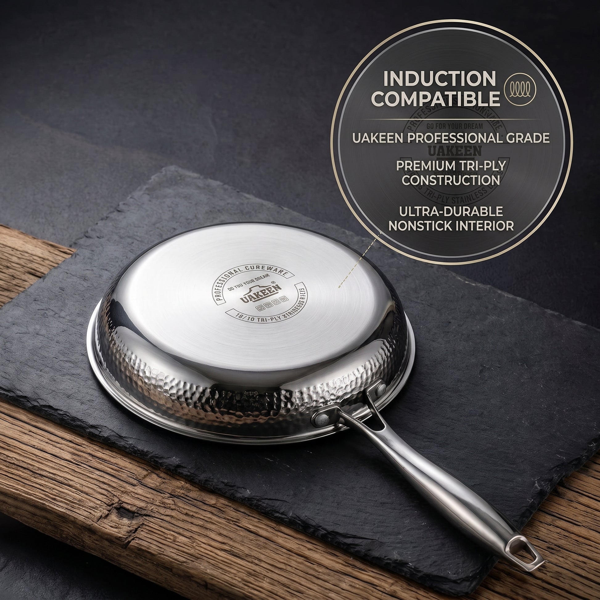 A Uakeen stainless steel frying pan shown upside down on a dark slate board over a wooden surface, with a circular callout in the upper right stating 'Induction Compatible' and product features.