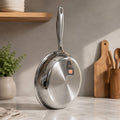 A stainless steel frying pan with a hammered texture on the bottom half and a polished finish on the rim, standing on a marble countertop in a kitchen setting.